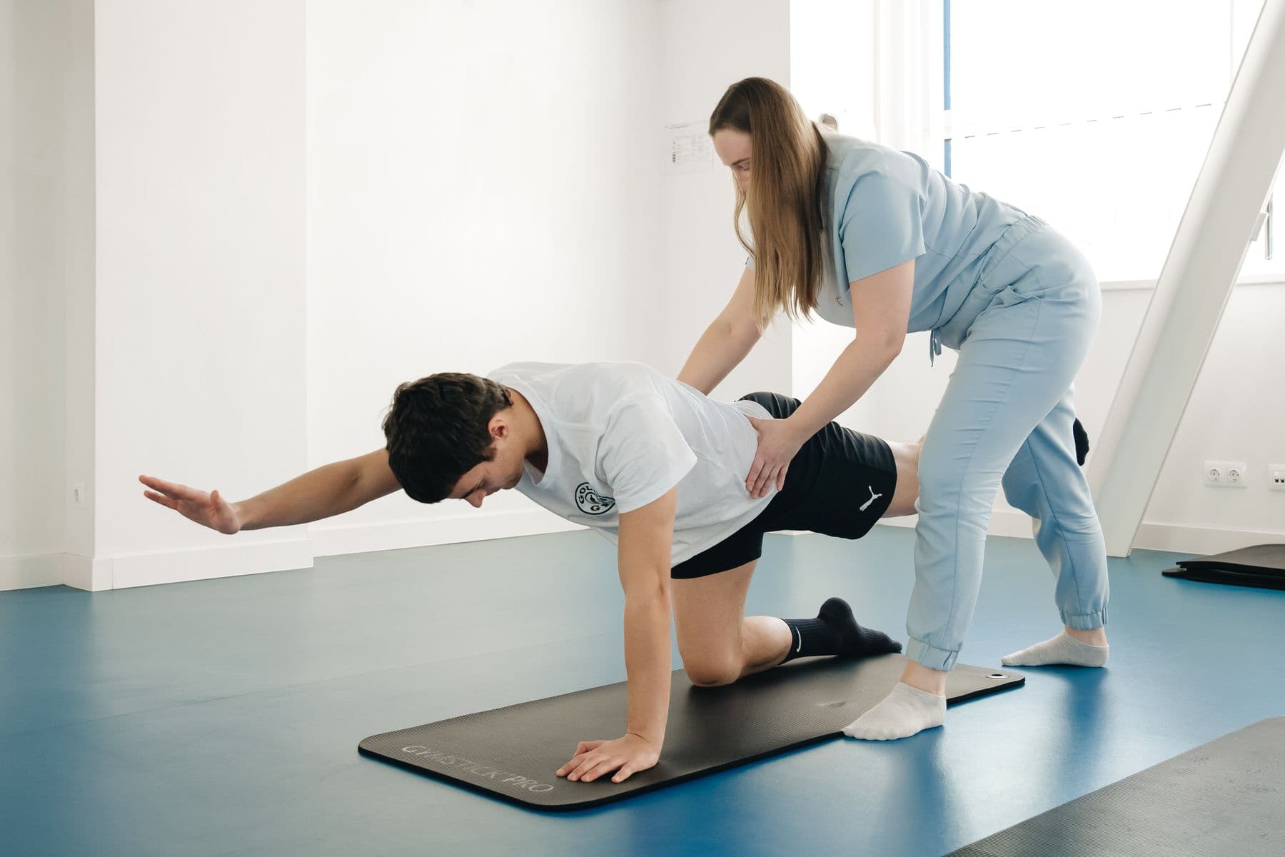 Physiotherapist spotting a patient through a floor rehab exercise on a mat