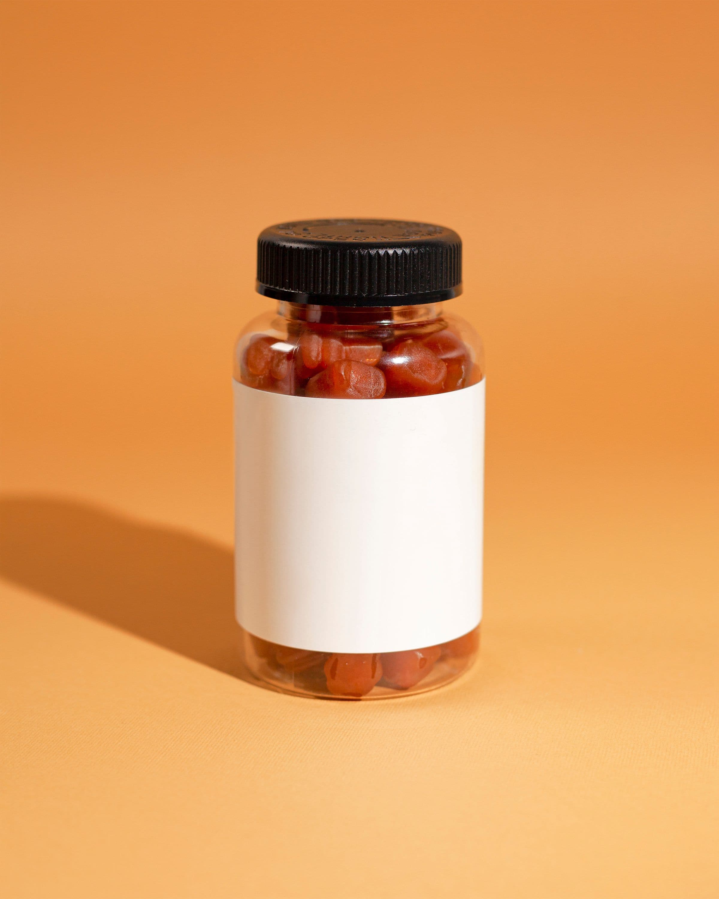 Clear bottle of red gummies with a blank label and a black cap, a candy-like supplement format