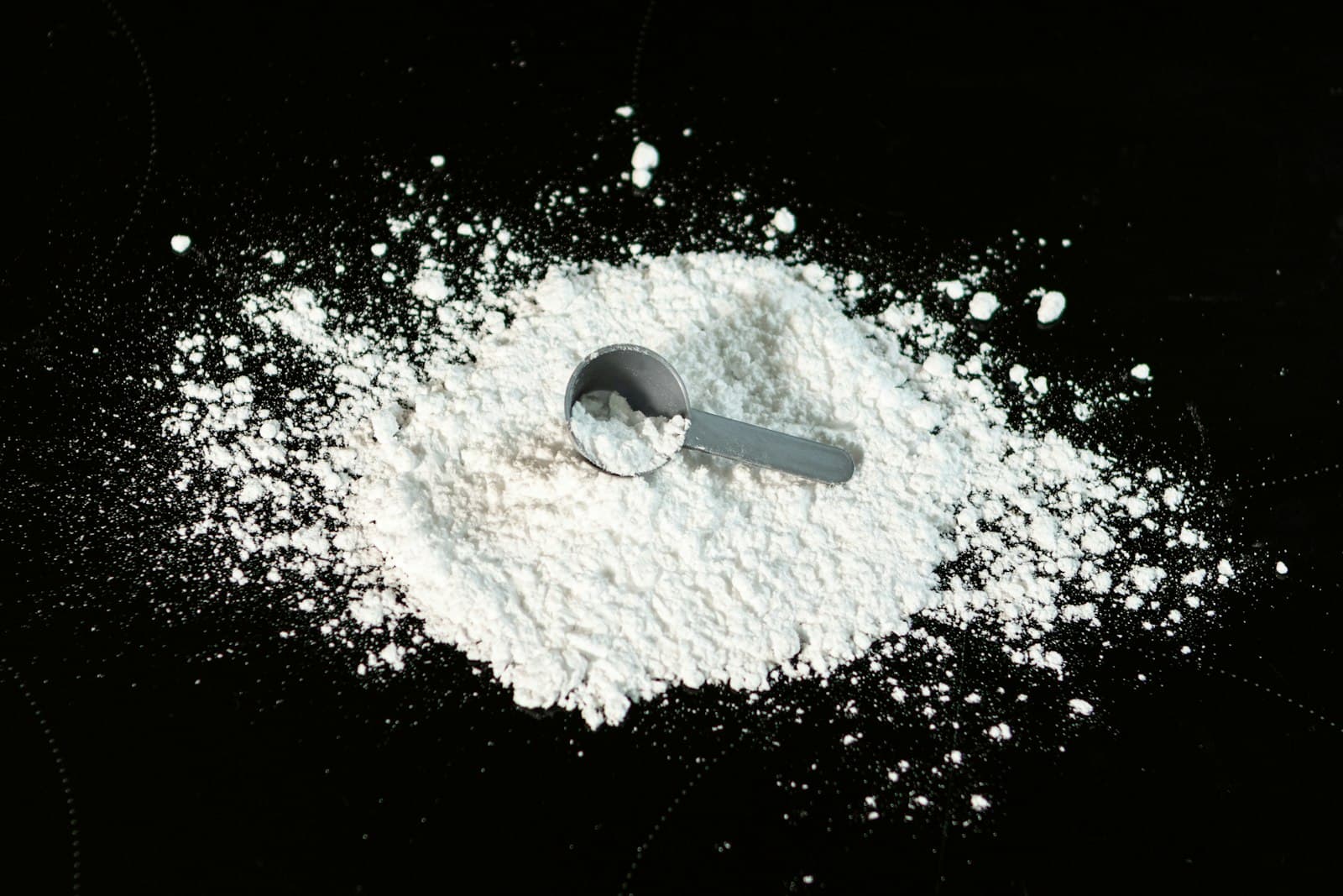 Gray scoop sitting in a pile of dry white powder on a black studio background