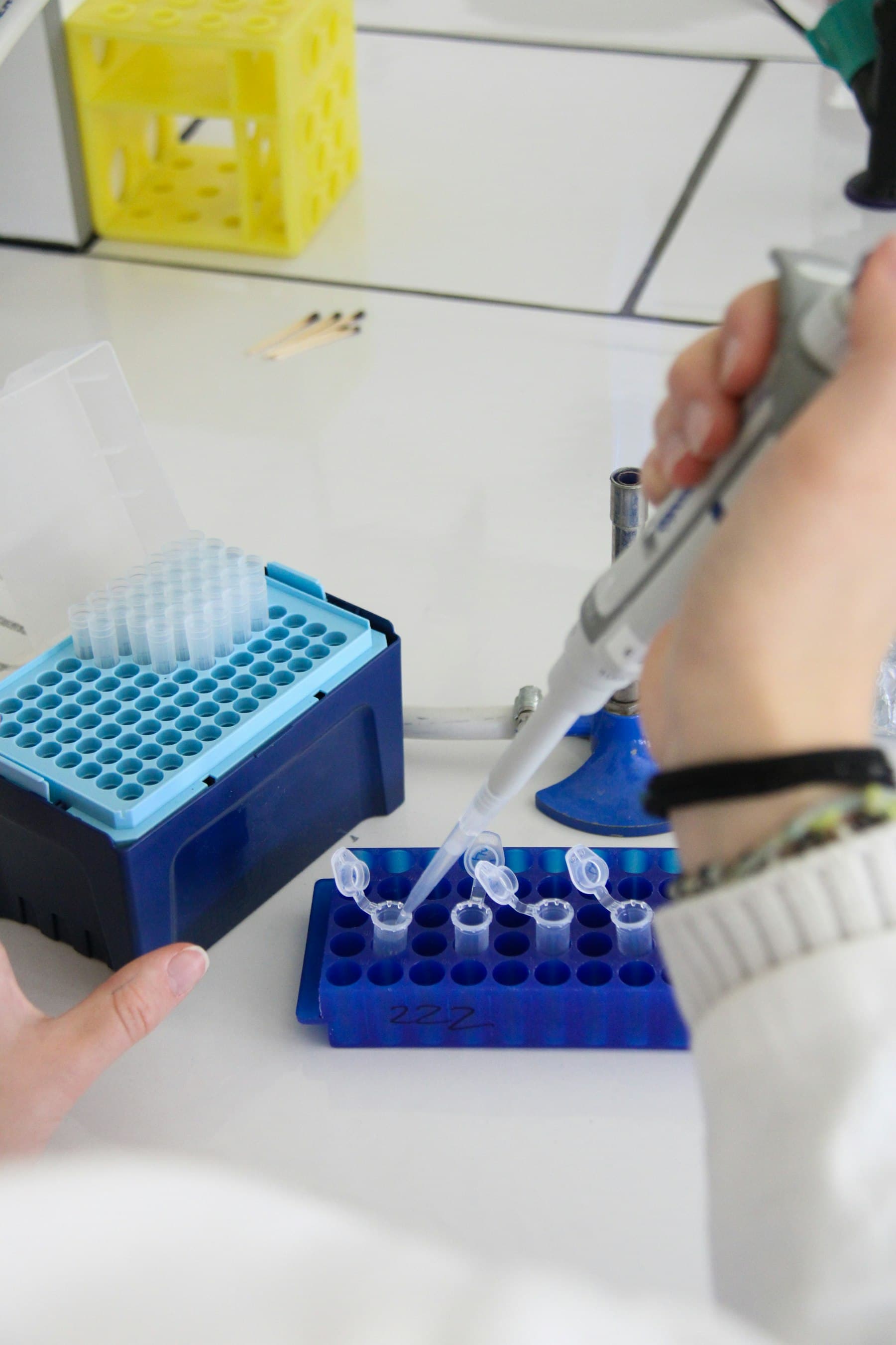 Hands in a white lab coat using a micropipette over a rack of microtubes