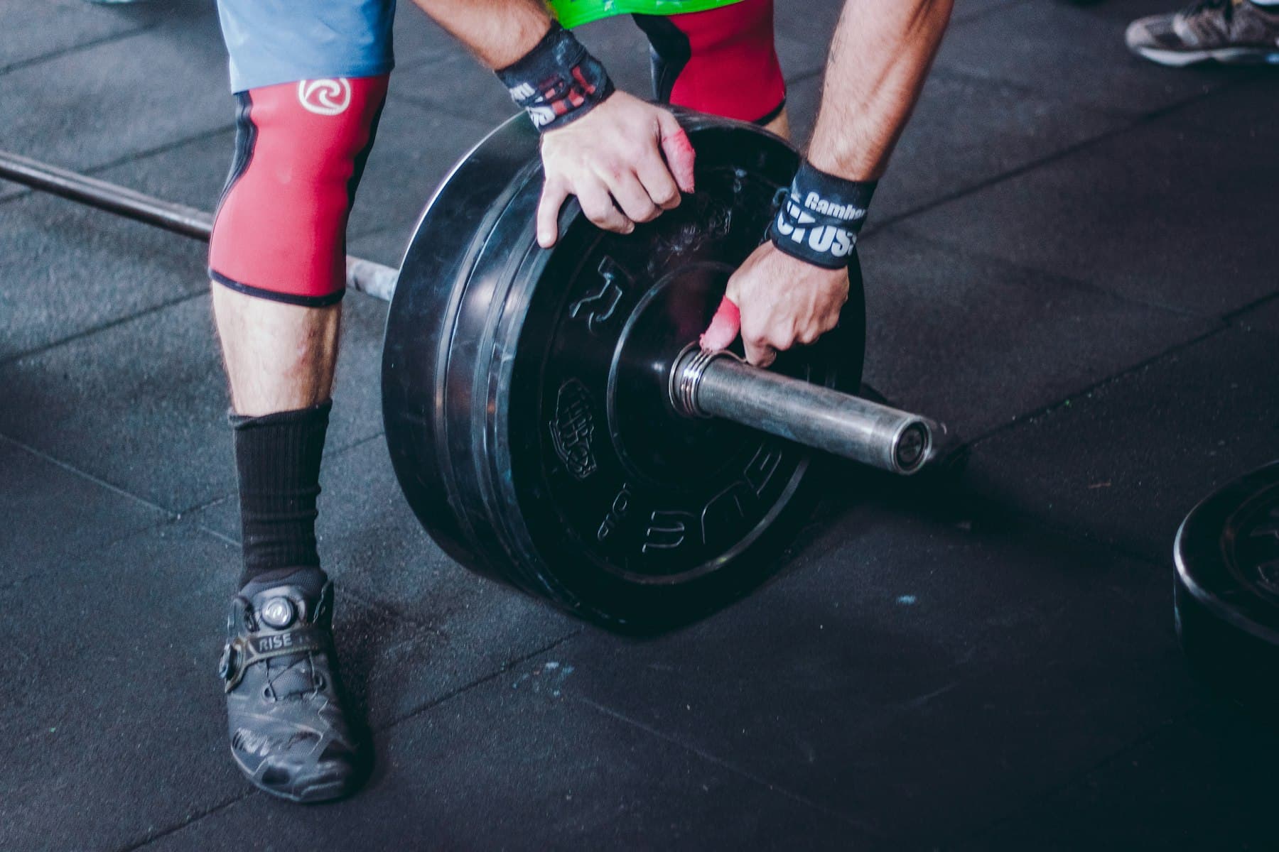 Hands loading a barbell plate on a gym floor before a lift