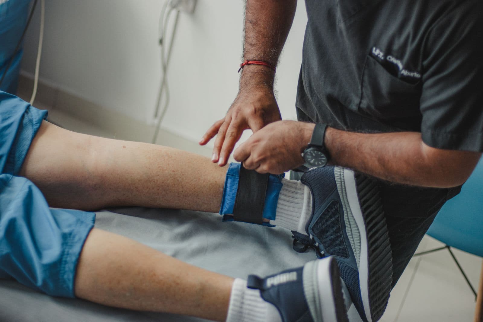 Clinician fastening a blue ankle strap on a patient's lower leg during a clinical rehab session