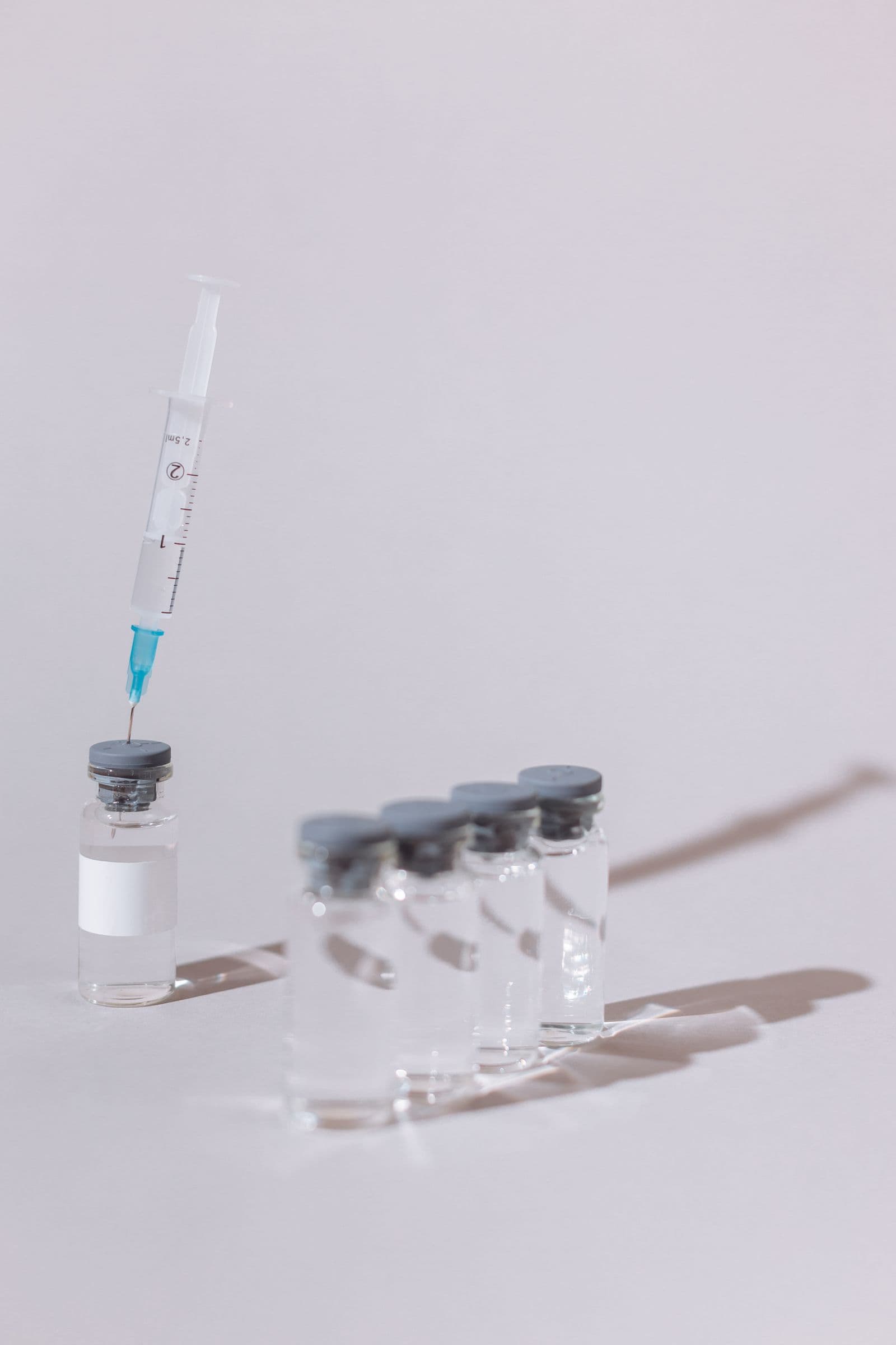 Syringe standing in a small glass vial beside a row of unlabeled research vials
